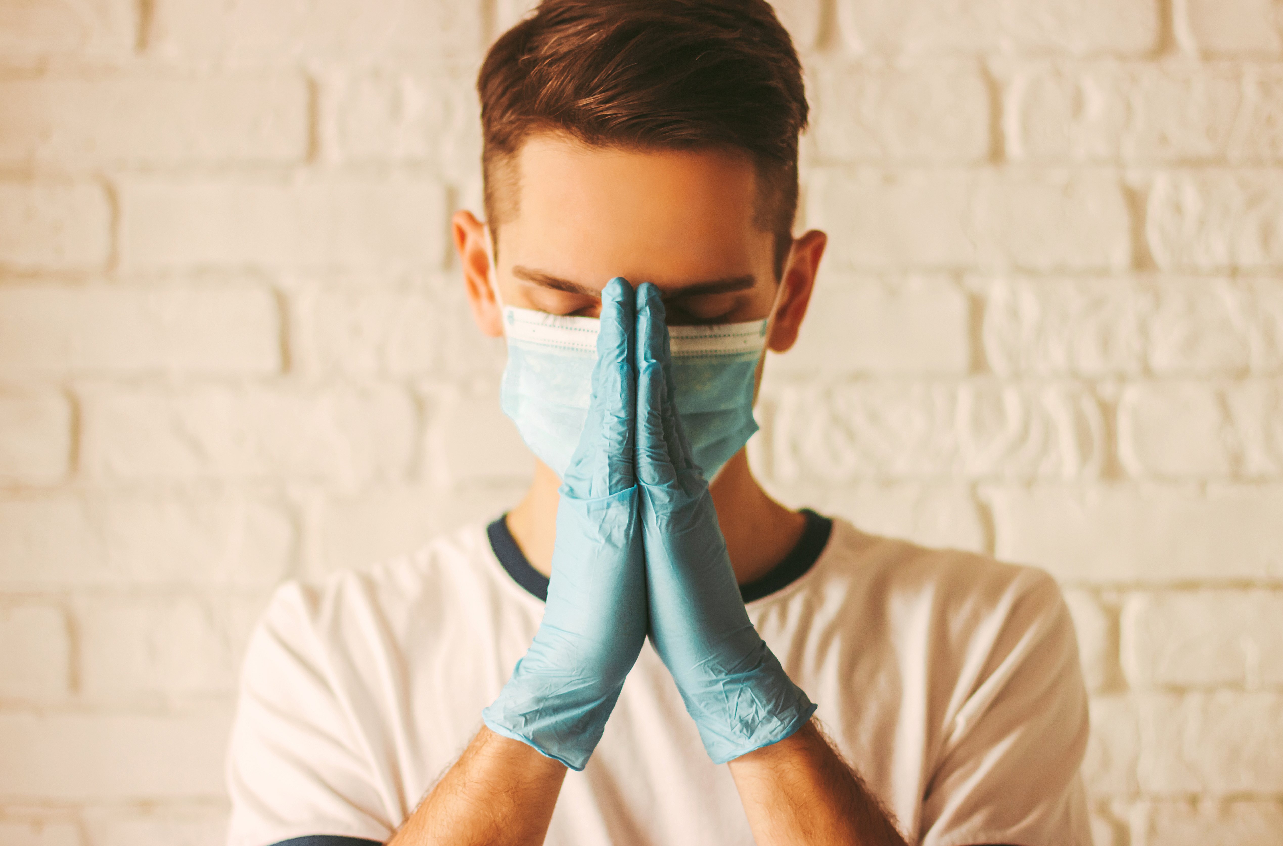 Joven doctor reza con mascarilla y guantes en un hospital