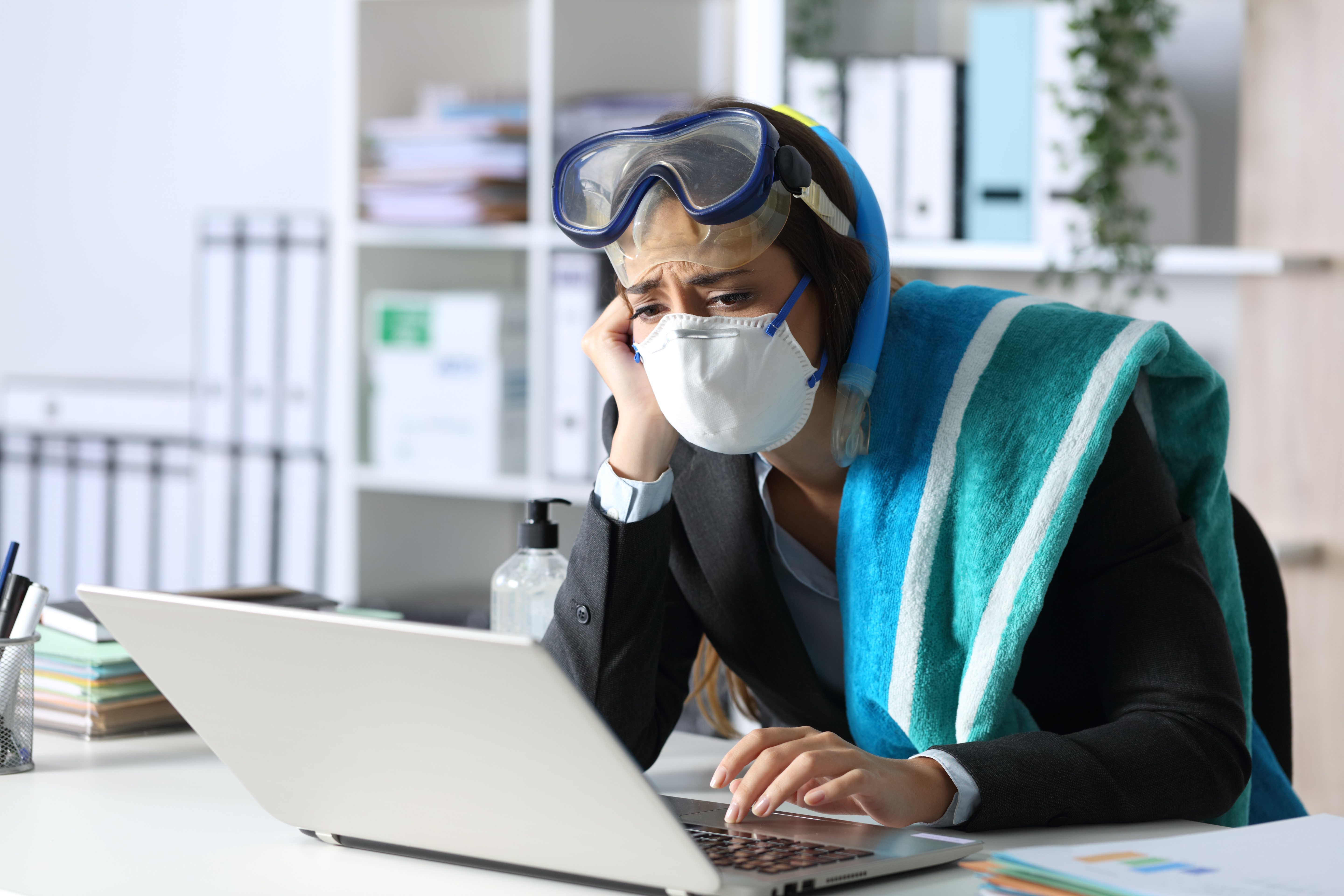 Triste mujer ejecutiva con máscaras cancelando vacaciones en una laptop en la oficina usando gafas y toalla