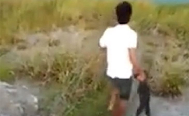 El chico agarra del cuello al perro y lo lanza al lago