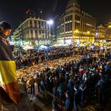 Un joven envuelto en la bandera belga deja una vela en el memorial de Bruselas