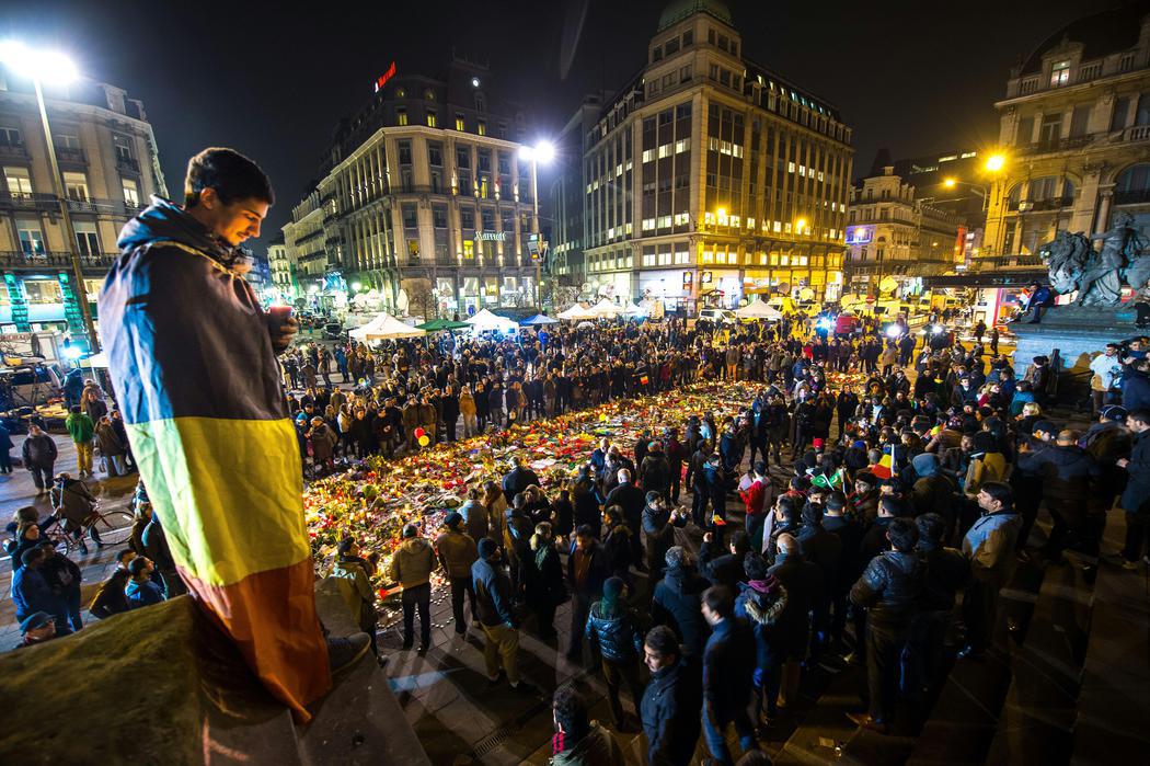 Un joven envuelto en la bandera belga deja una vela en el memorial de Bruselas